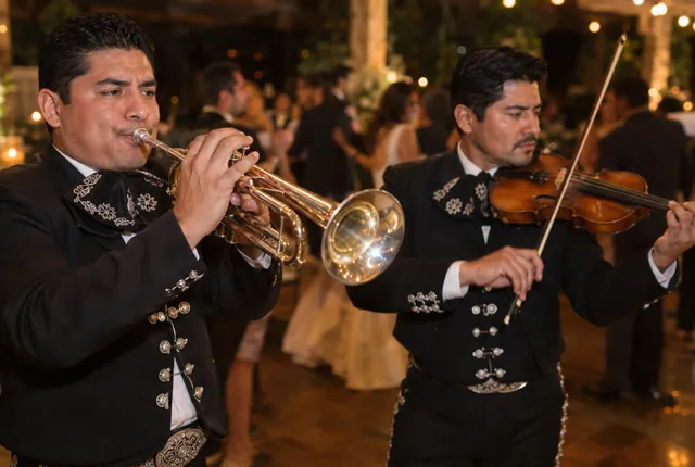 A trumpet player and a violinist in charro suits play at an evening wedding reception.