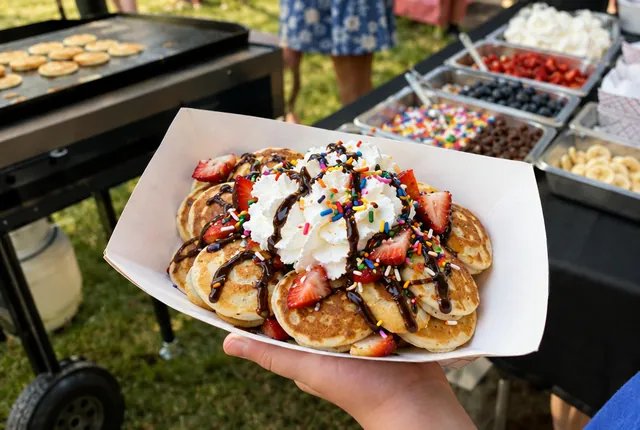 A paper boat of mini pancakes with strawberries, whipped cream, chocolate and sprinkles.